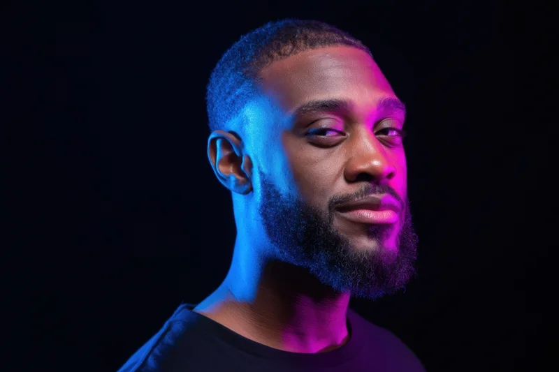 Close-up portrait of a man with a neatly trimmed beard under blue and pink neon lighting in a dark studio
