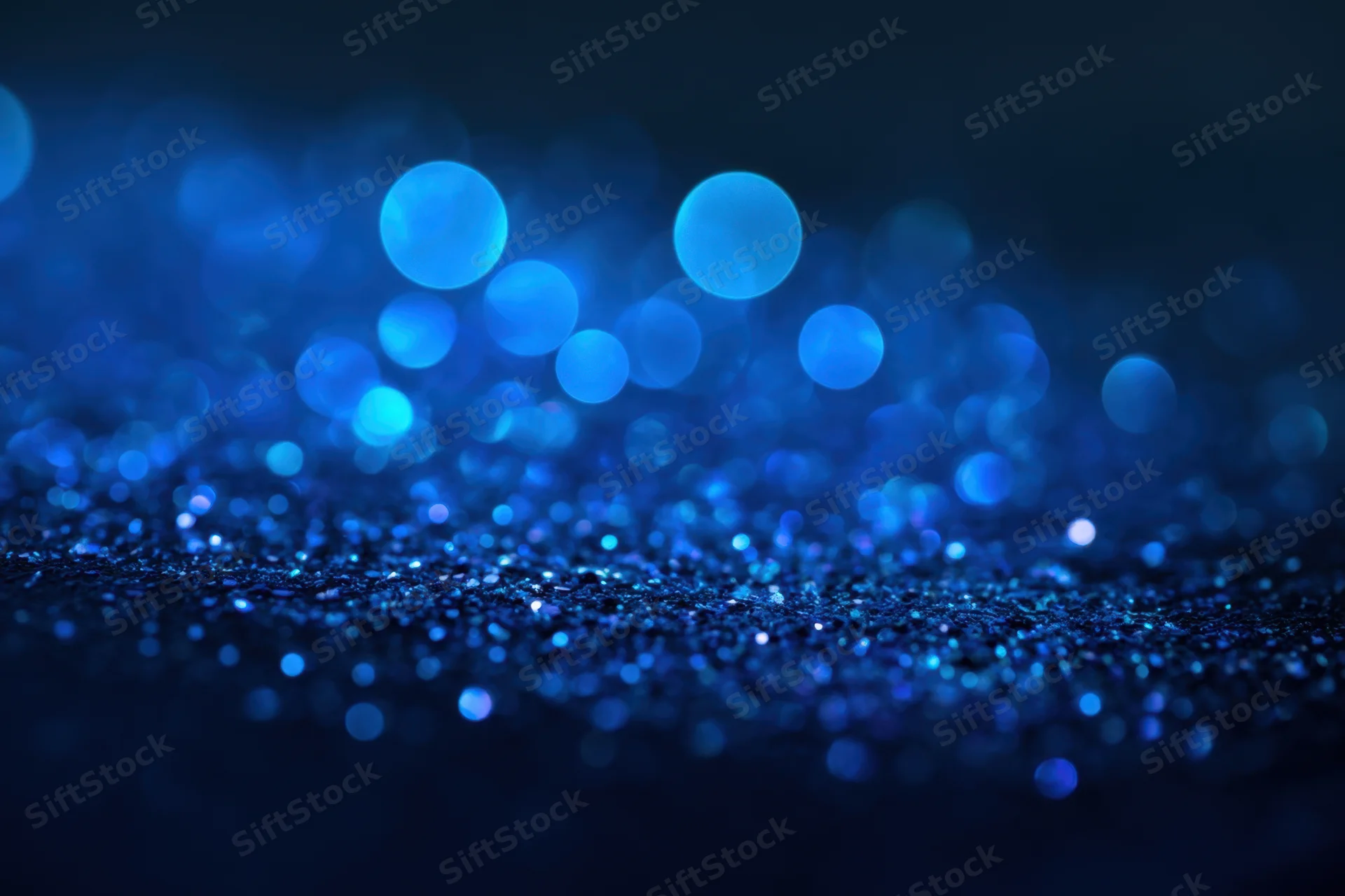 Blue glitter particles sparkling on a dark surface with bokeh lights in the background