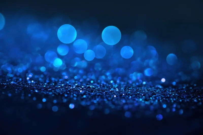 Blue glitter particles sparkling on a dark surface with bokeh lights in the background