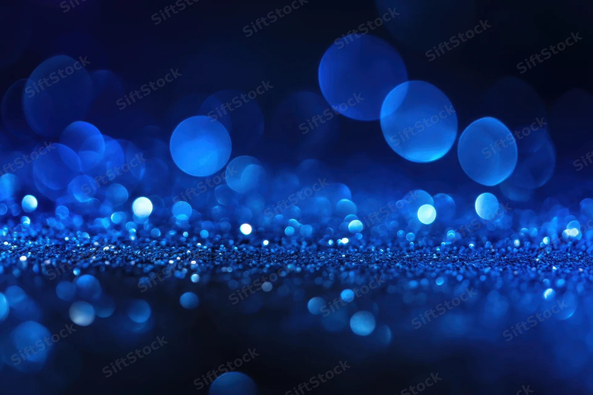 Blue glitter particles sparkling on dark surface with bokeh lights in background