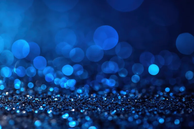 Blue glitter particles sparkling on a dark surface with bokeh lights in the background
