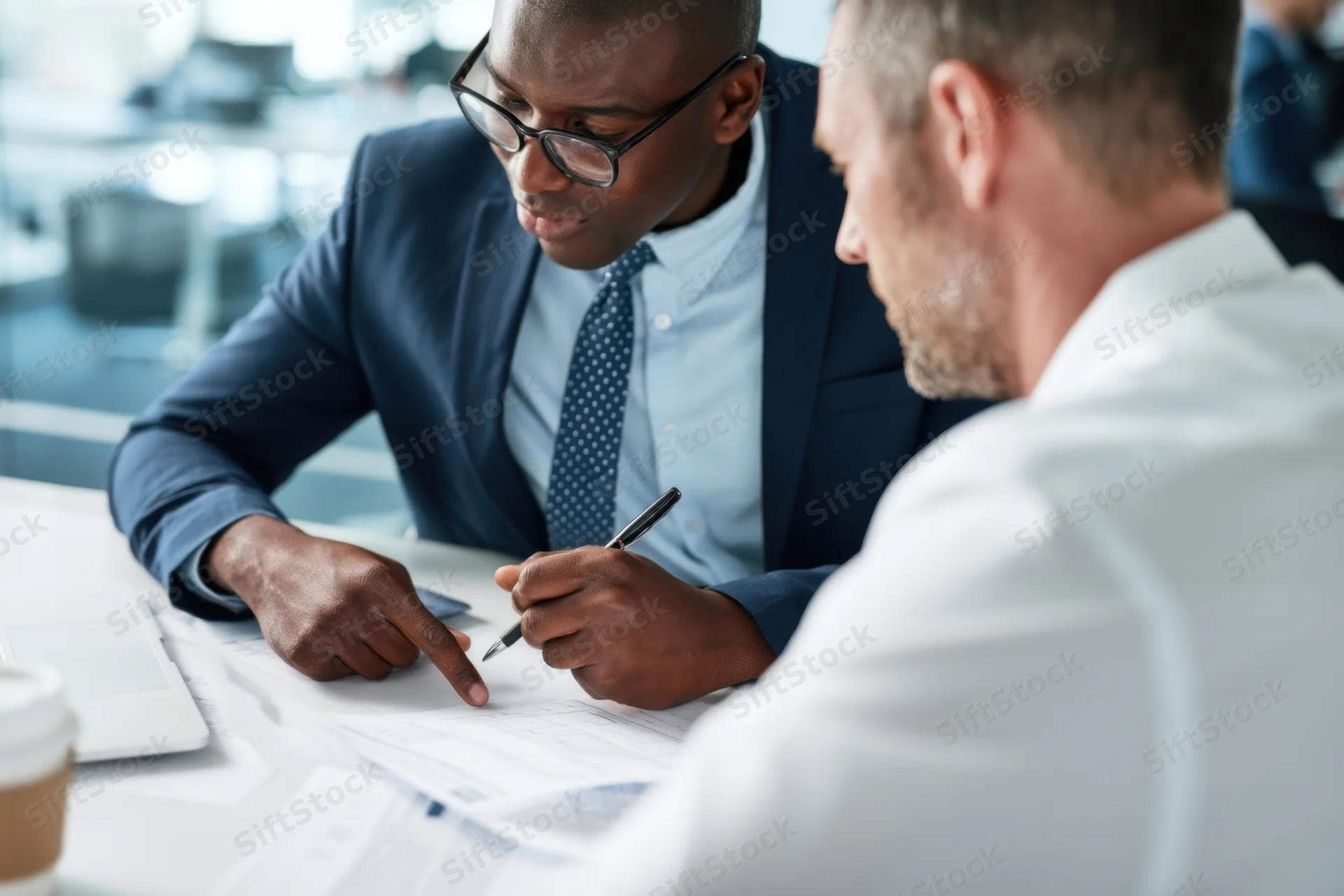 Two men in business attire discussing documents at a desk in an office