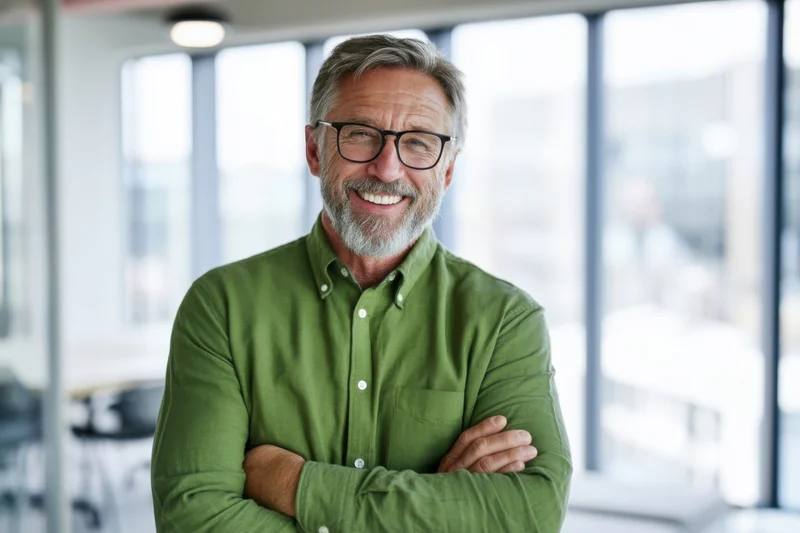 Middle-aged man with glasses smiling with arms crossed in a bright modern office