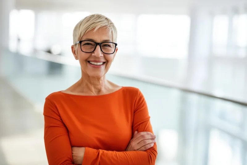 Senior woman smiling with arms crossed in modern office interior