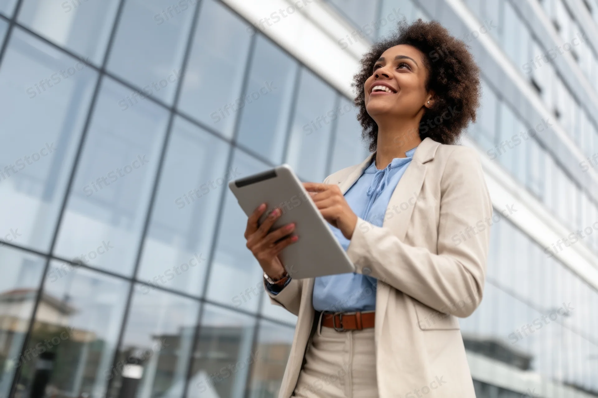 Woman in business attire holding tablet outside modern glass building