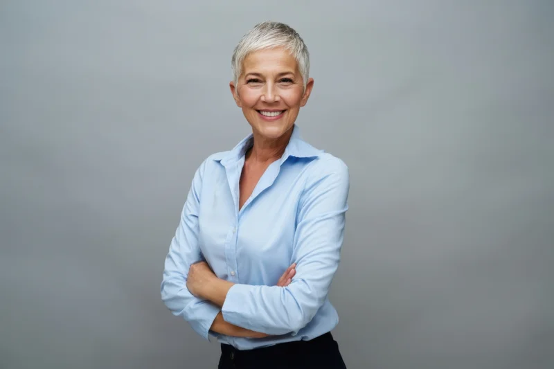 Senior woman with short gray hair standing confidently with arms crossed in a studio setting