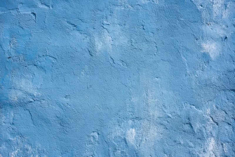 Textured blue plaster wall with rough surface and subtle white patina