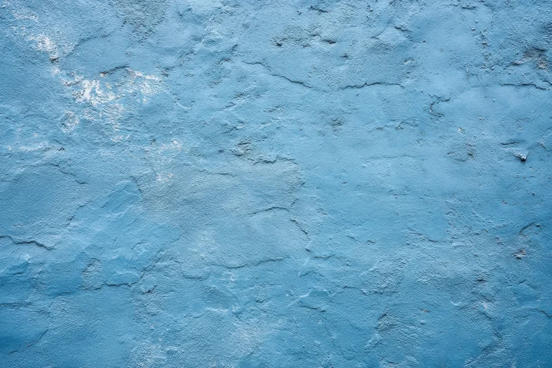 Textured blue plaster wall with cracks and peeling paint