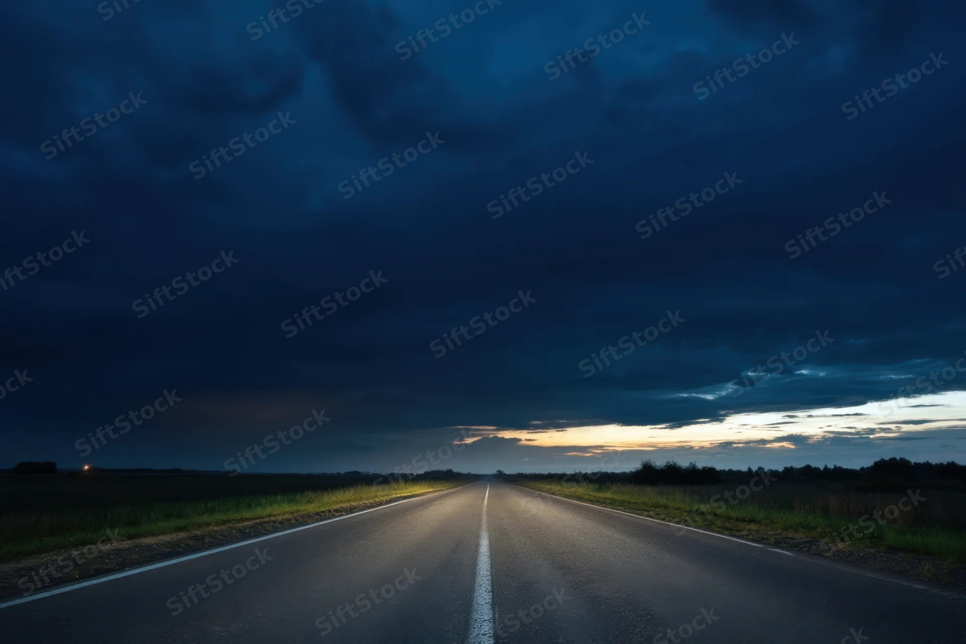 Straight asphalt road stretching into the horizon under a dark cloudy sky at twilight