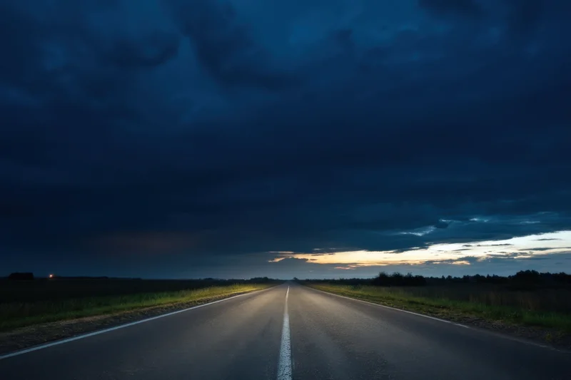 Straight asphalt road stretching into the horizon under a dark cloudy sky at twilight