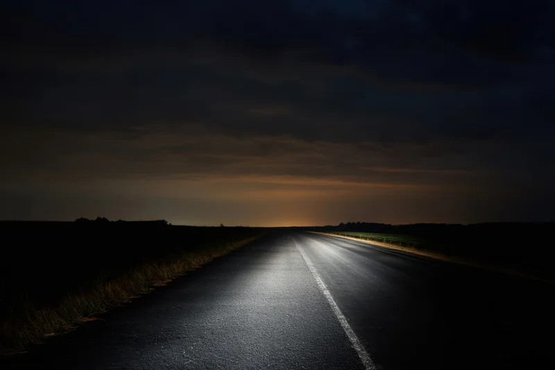 Illuminated asphalt road stretching into the horizon under a dark cloudy night sky