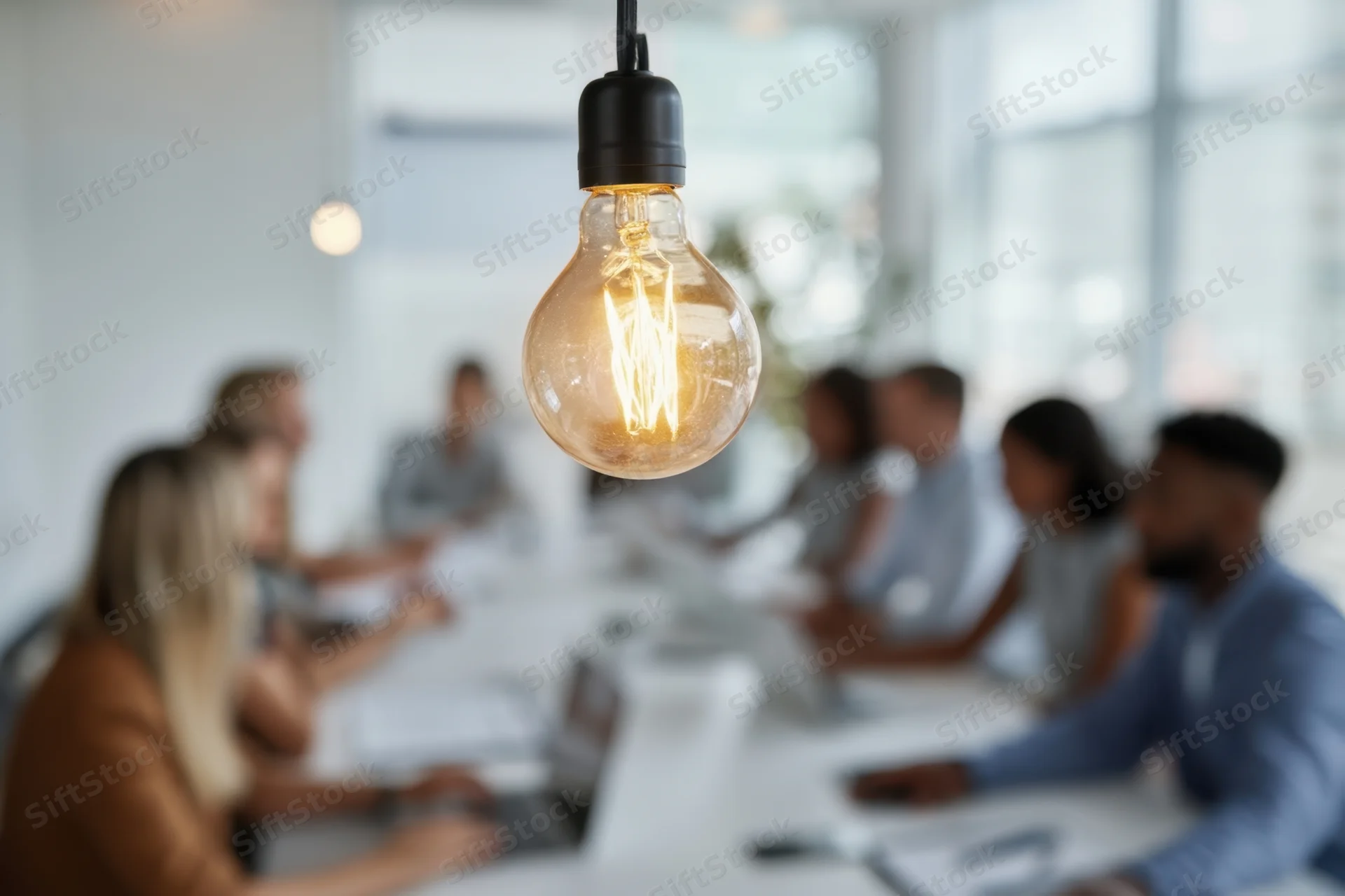 Glowing lightbulb in focus above a diverse group of professionals in a conference meeting at a long table in a modern office