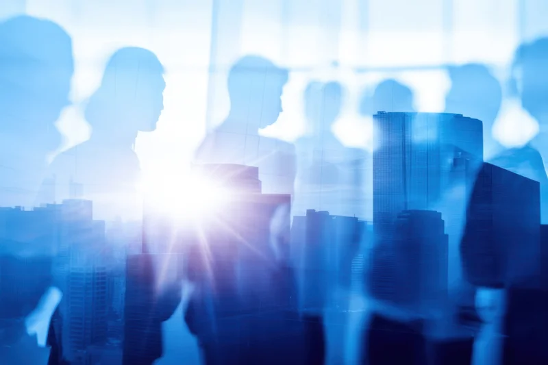 Translucent silhouettes of professionals overlaid on a sunlit city skyline viewed through an office window