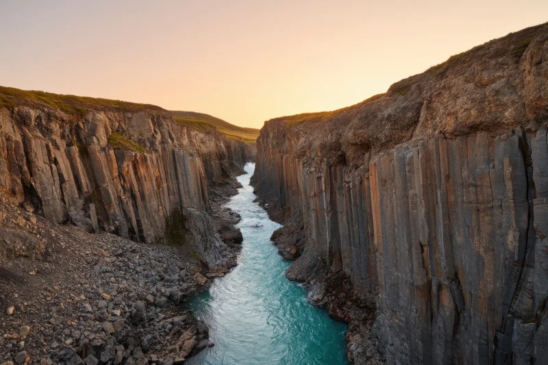 Hexagonal basalt columns lining a narrow river canyon at sunset