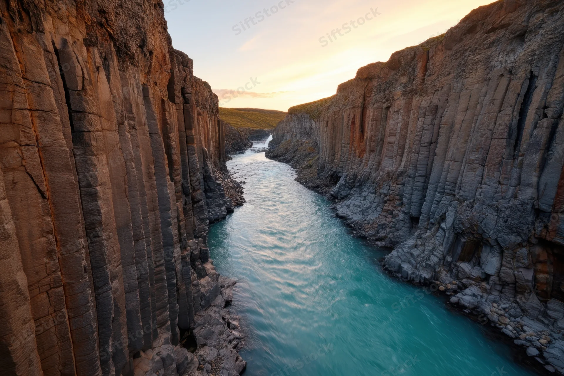 Hexagonal basalt columns lining a river canyon at sunset