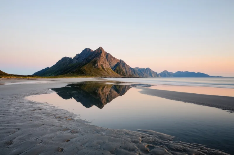 Jagged mountain peaks reflected in still water at a sandy beach during sunset