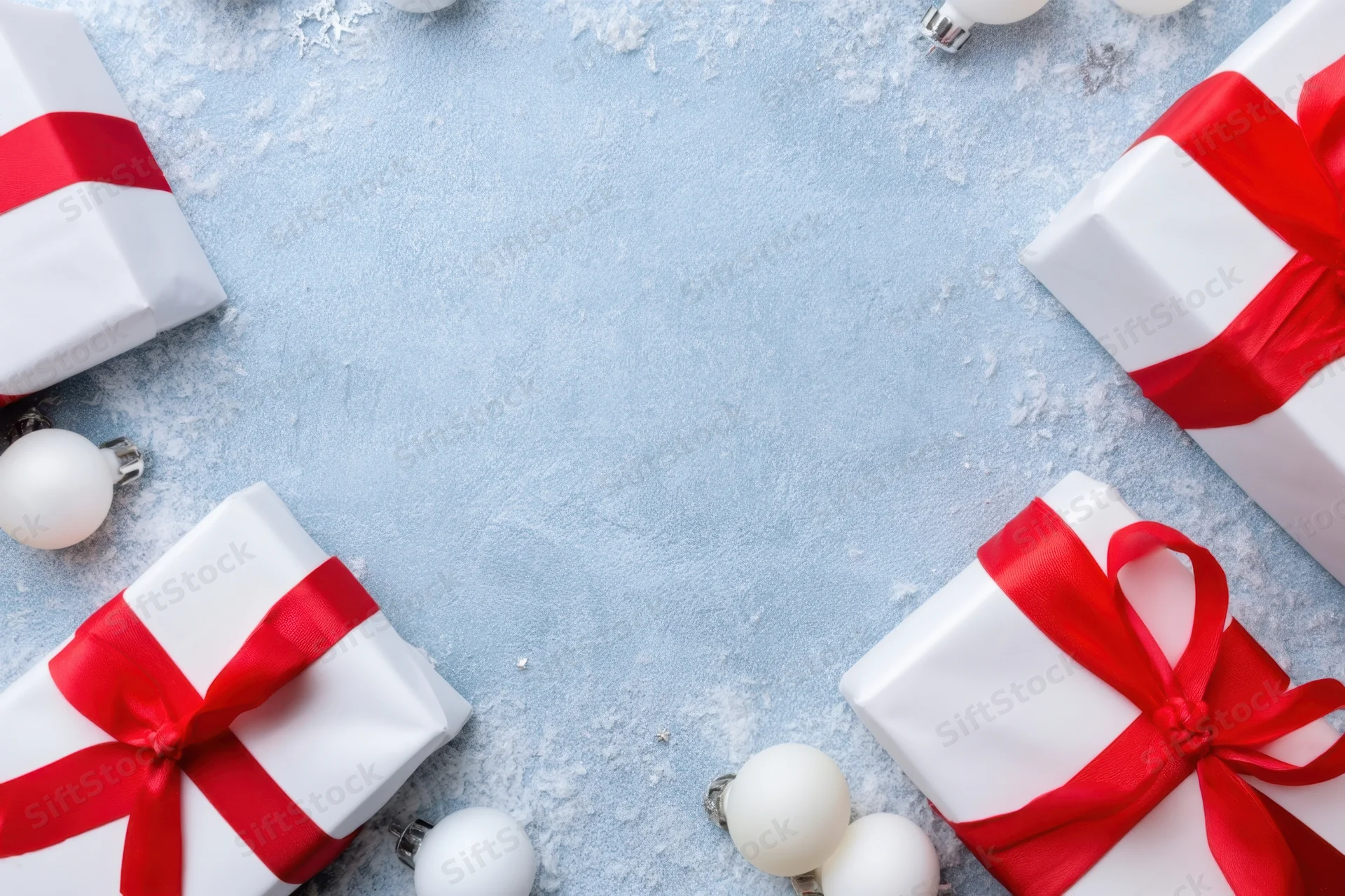White gift boxes with red ribbons and ornaments arranged on a snowy blue surface with copyspace