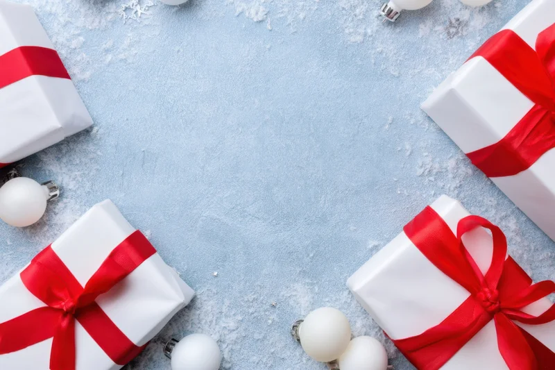 White gift boxes with red ribbons and ornaments arranged on a snowy blue surface with copyspace