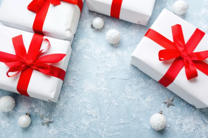 White gift boxes with red ribbons and holiday ornaments arranged on a snowy blue surface