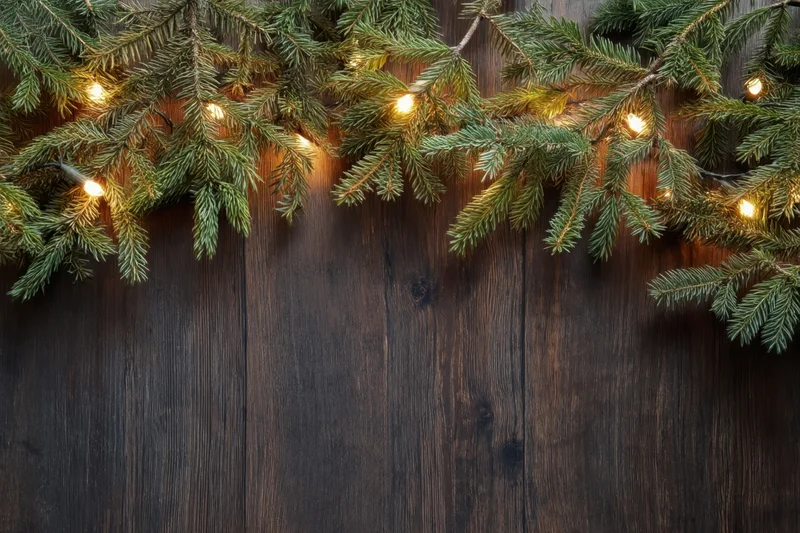 Evergreen branches with warm glowing lights arranged across dark wooden surface