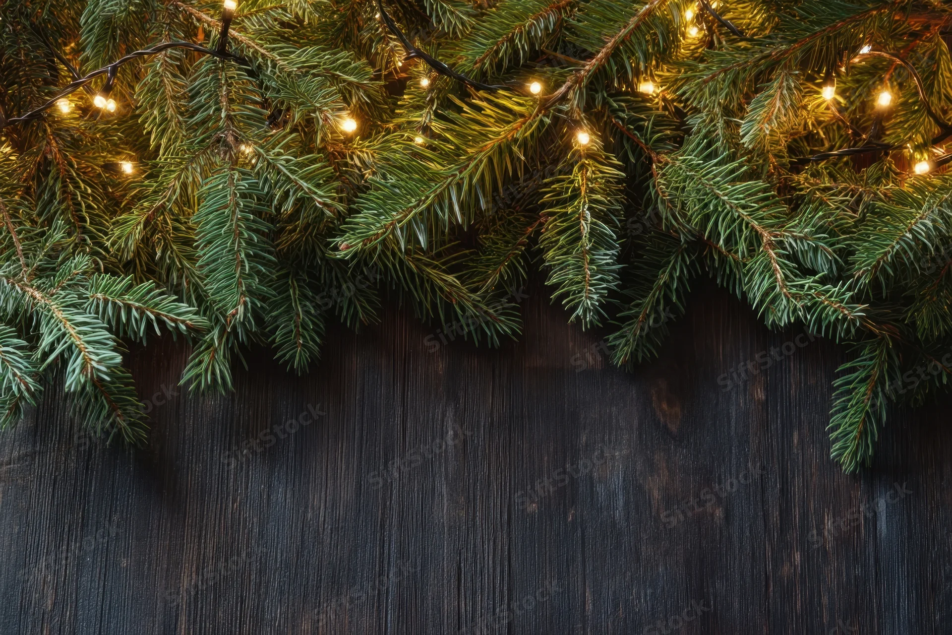 Evergreen branches with warm glowing lights arranged across dark wooden surface