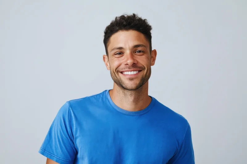 Smiling man in blue tshirt posing in studio with light background