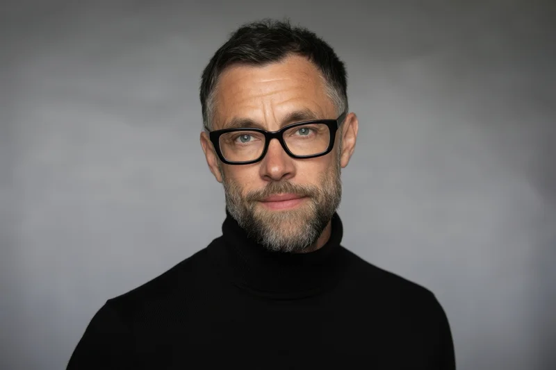 Man with glasses and beard wearing black turtleneck in studio portrait