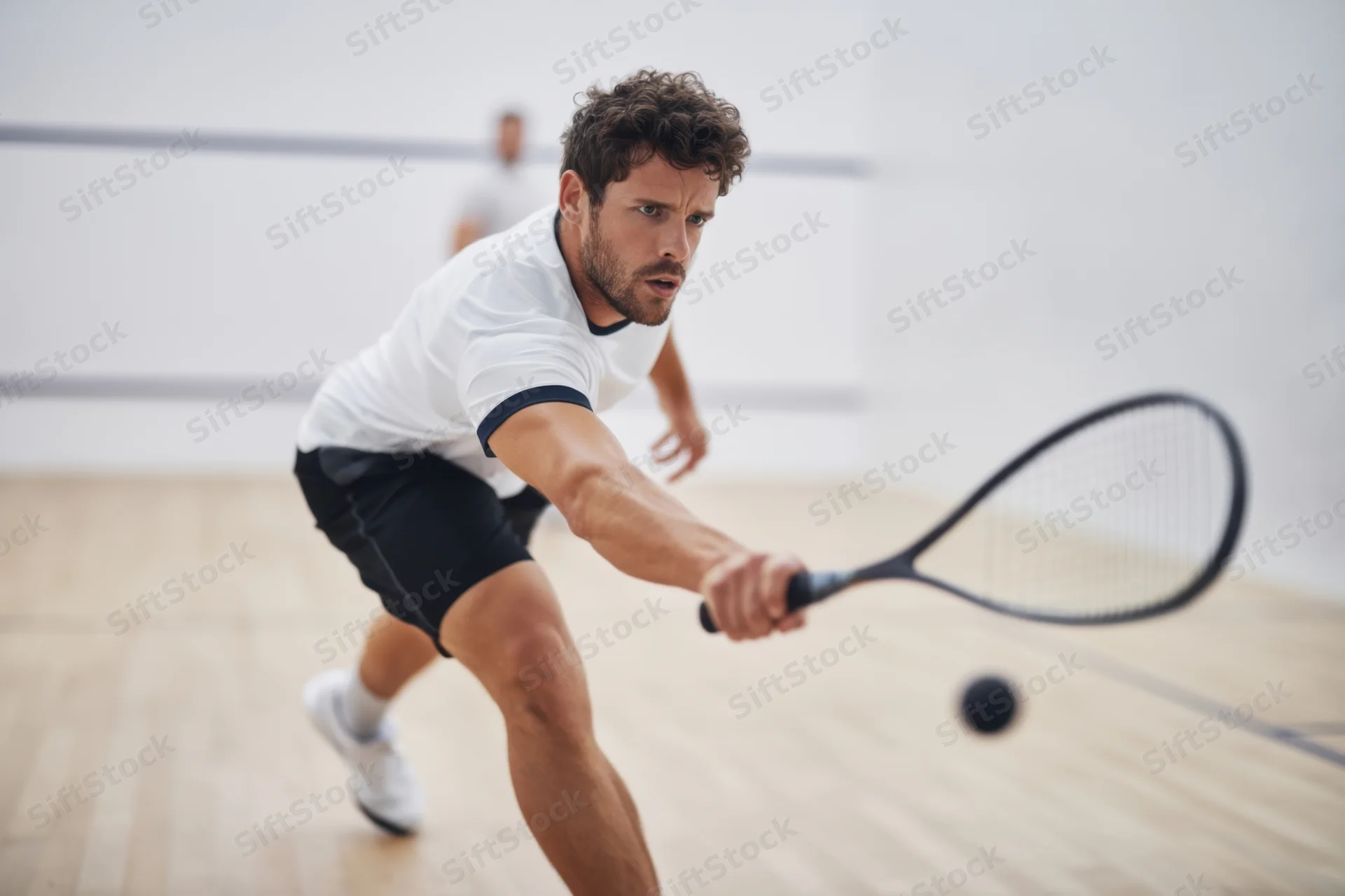 Male squash player hitting ball with racquet on indoor court
