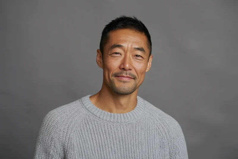 Asian man in light gray knitted sweater smiling at camera in studio portrait