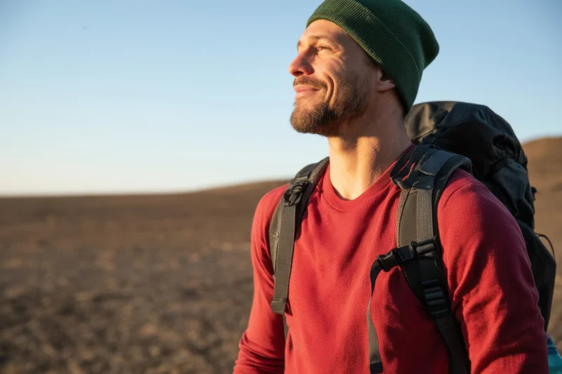 Man with backpack smiling while hiking in desert landscape