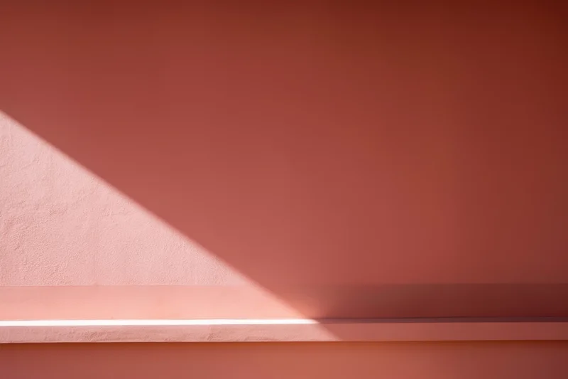 Diagonal beam of light casting shadow on warm pink wall in minimalist interior