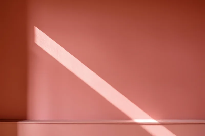 Diagonal beam of sunlight on warm pink wall in minimalist interior
