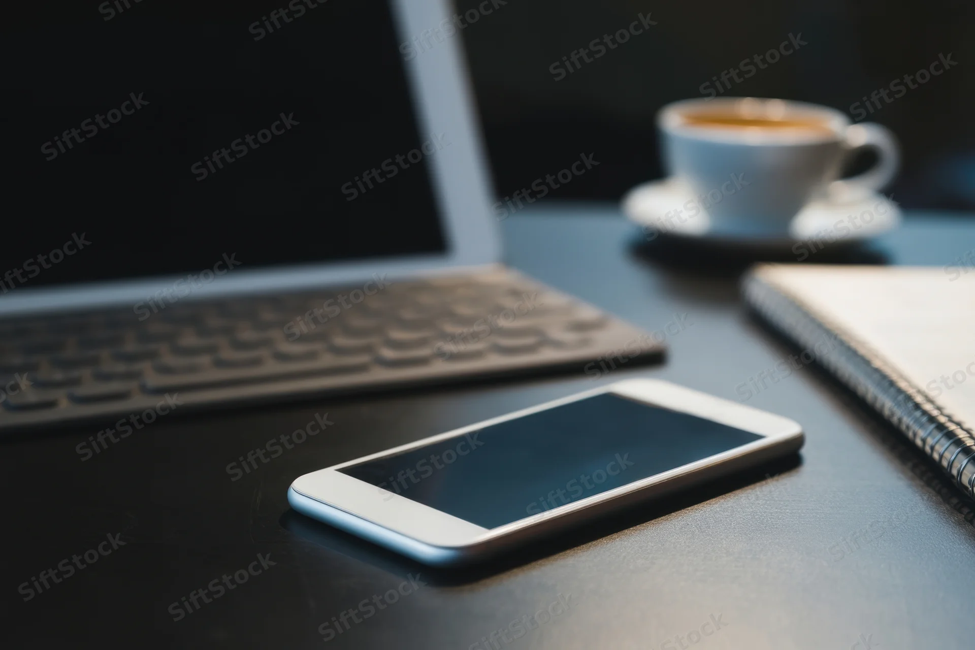 Tablet and smartphone on a dark desk beside a laptop, coffee cup and notebook