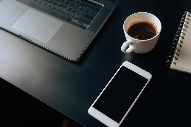 Dark desk with laptop, coffee mug, smartphone and notebook arranged for work