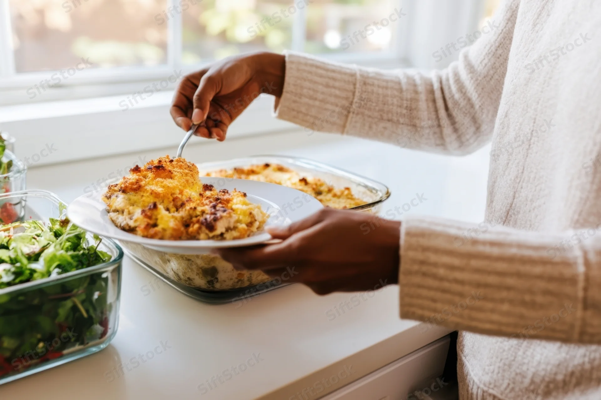 Woman serving baked casserole onto a plate in a bright kitchen