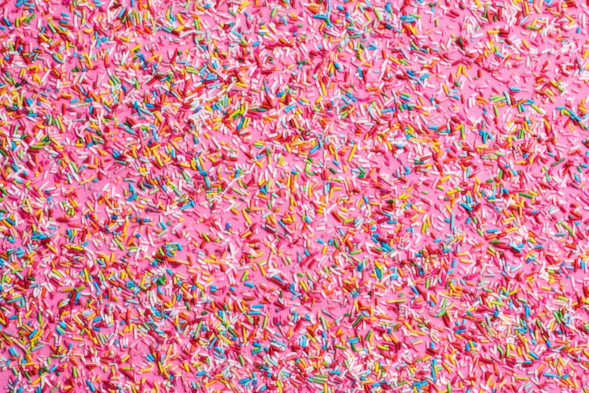 Multicolored candy sprinkles scattered across a pink surface