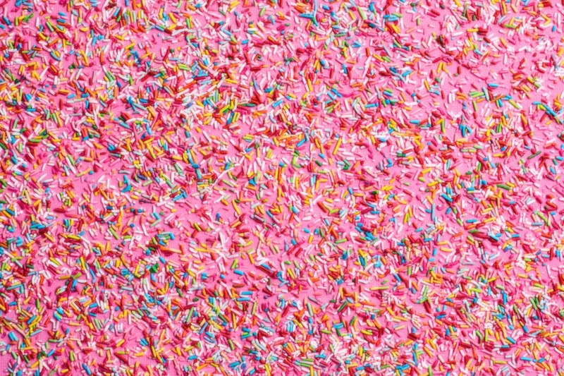 Multicolored candy sprinkles scattered across a pink surface