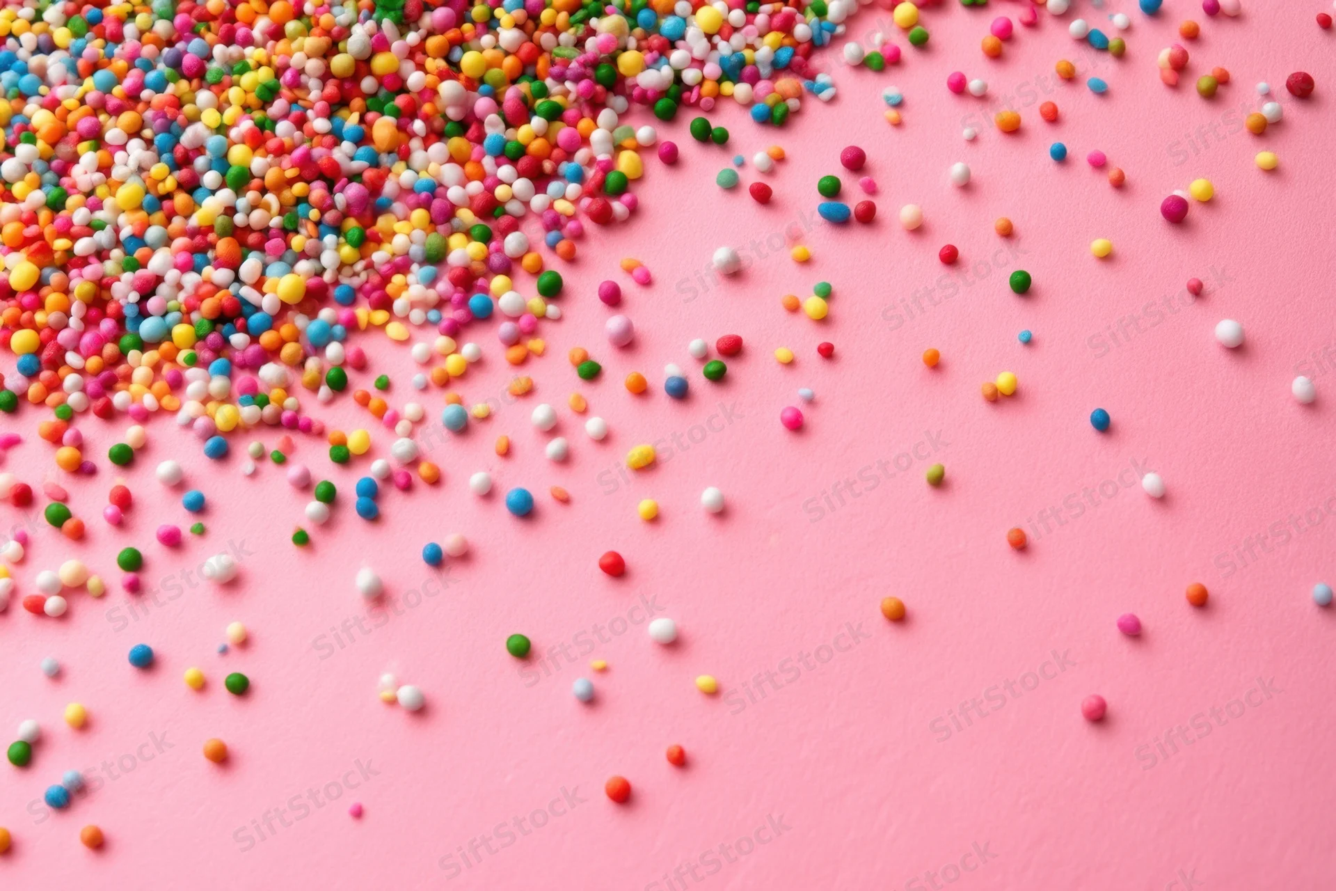 Multicolored candy sprinkles scattered across a pink surface with copyspace on the right