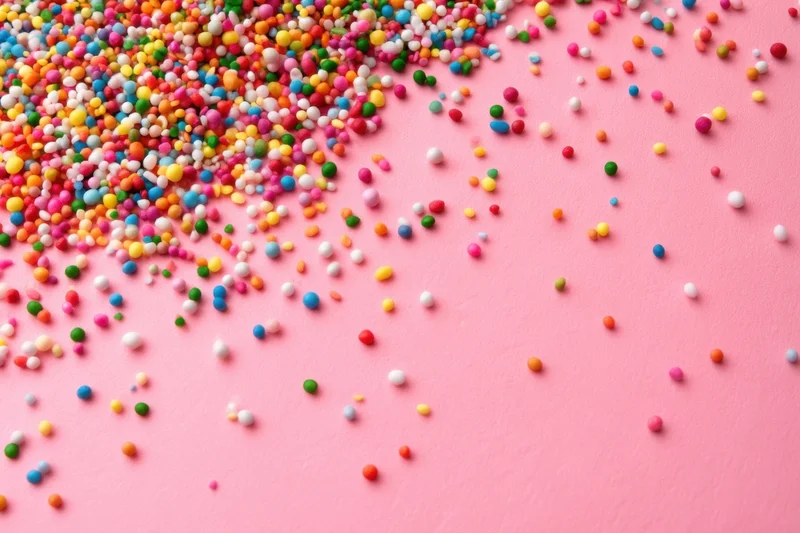 Multicolored candy sprinkles scattered across a pink surface with copyspace on the right