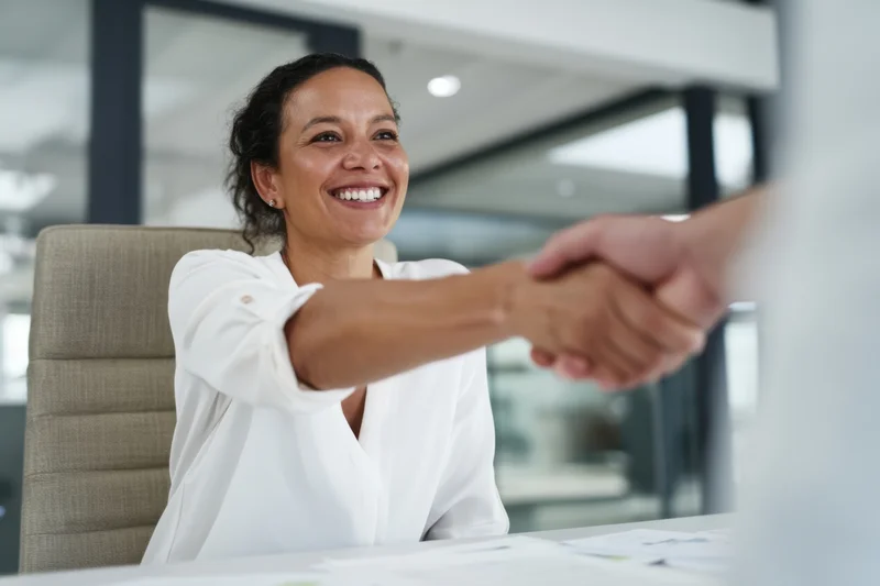 Woman in white blouse shaking hands at office desk smiling