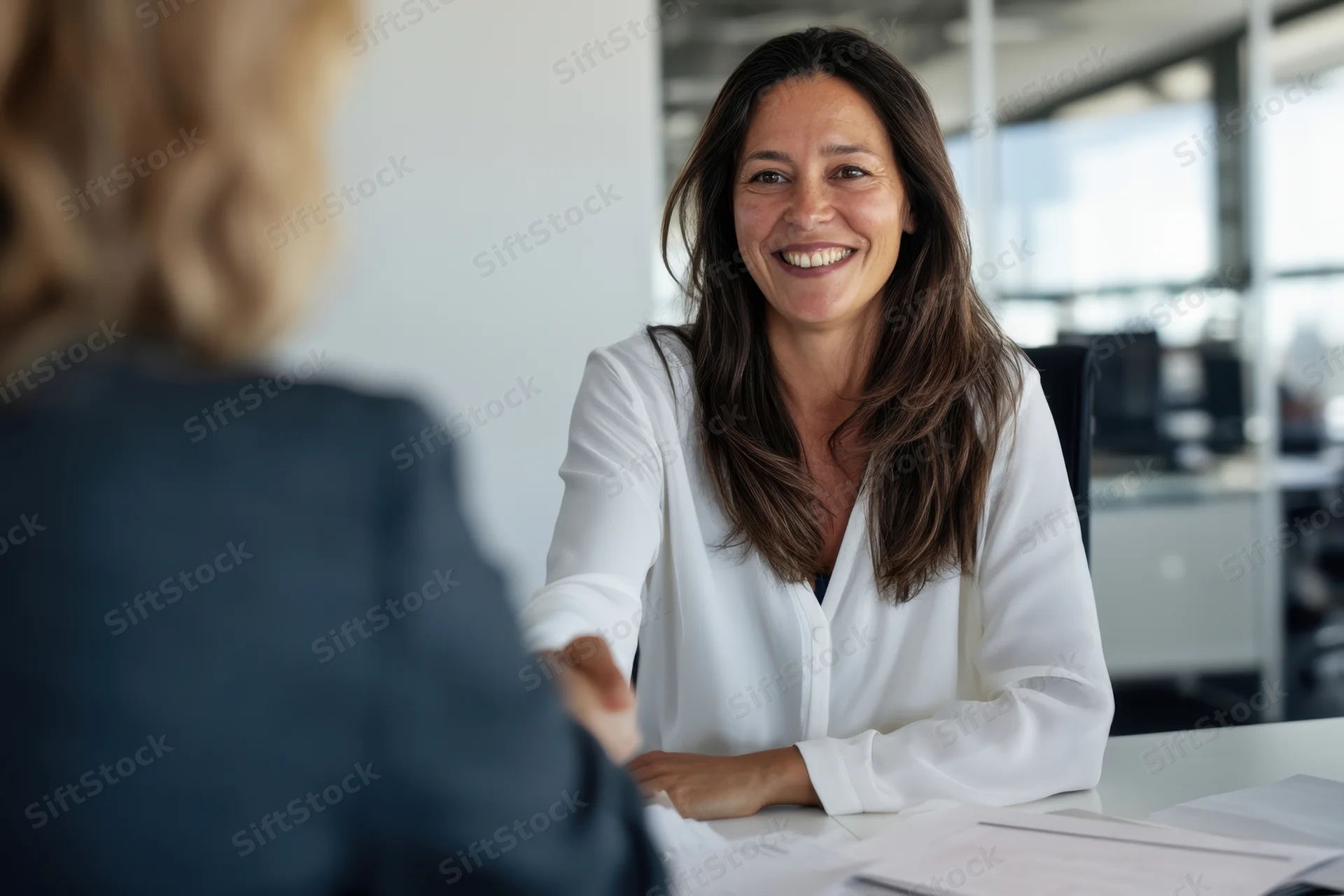 Woman in white blouse smiling during office meeting at desk
