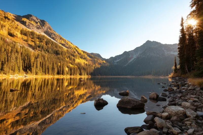 Alpine lake reflecting golden autumn forest and mountains at sunrise