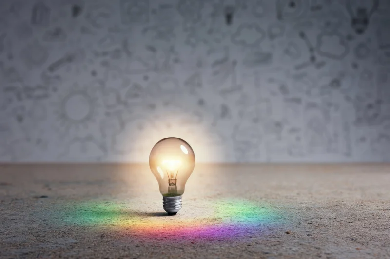 Glowing lightbulb on rough concrete surface with rainbow reflection and sketched background