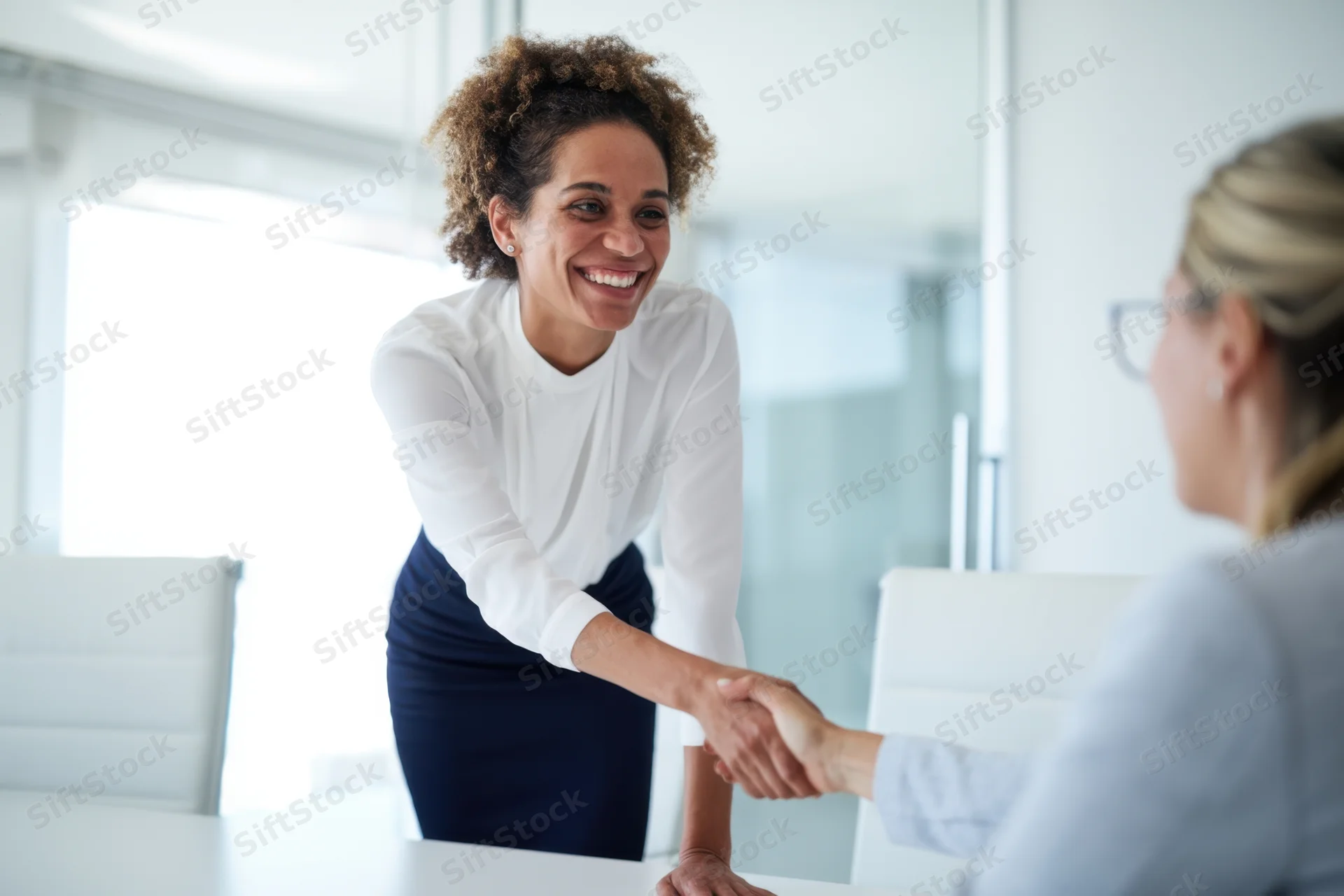 Smiling businesswoman shaking hands with colleague at office table
