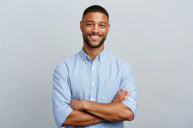 Smiling man with arms crossed wearing a blue button-down shirt against a plain background