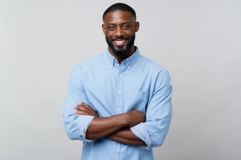 Smiling man with arms crossed wearing light blue button-down shirt in studio setting