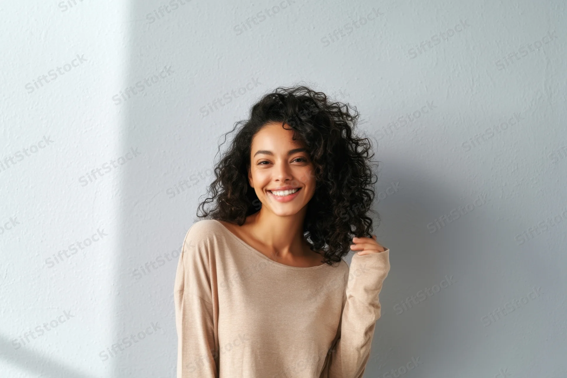 Smiling woman with curly black hair wearing beige longsleeve top indoors
