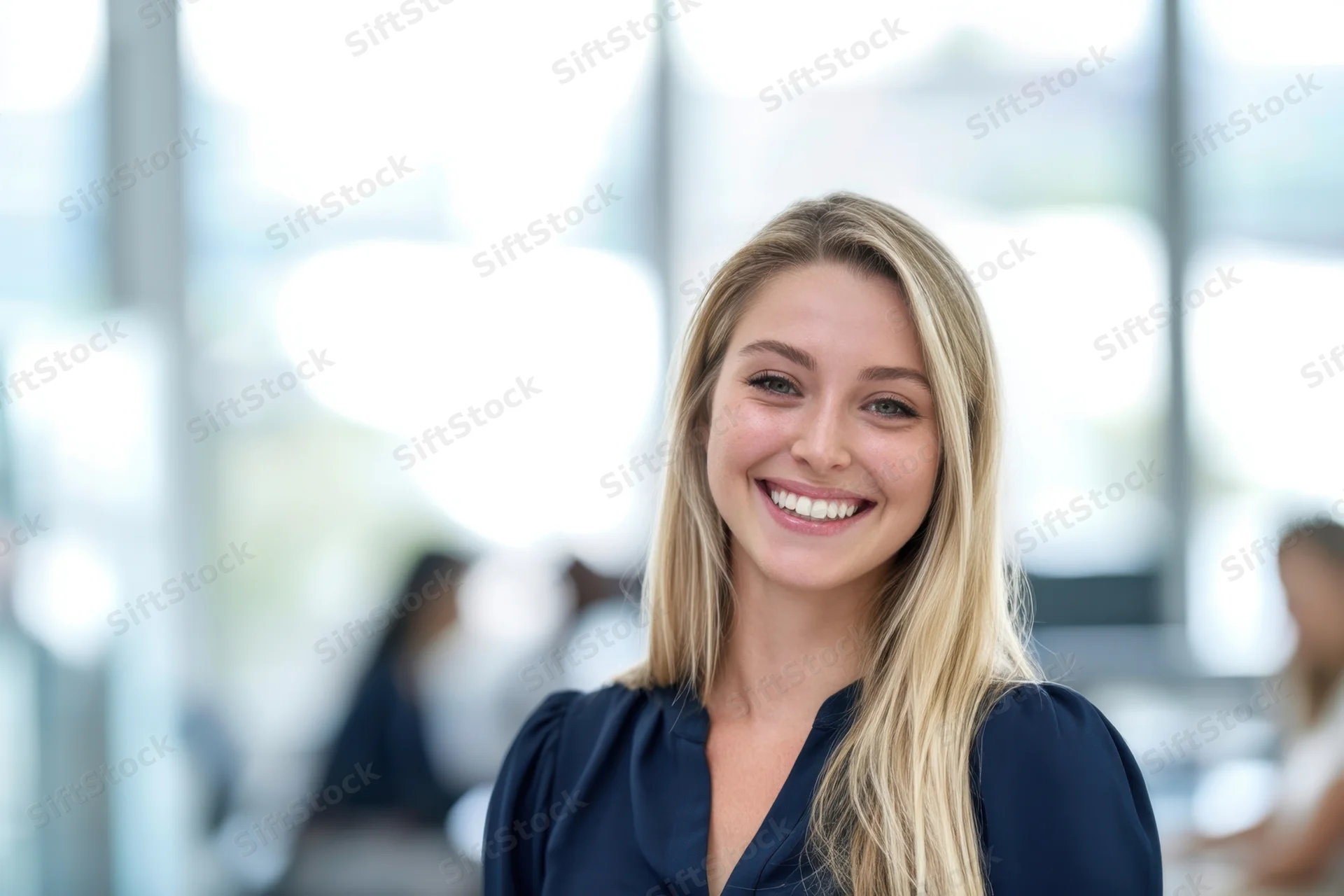 Smiling blonde woman in dark blue blouse standing in modern office interior