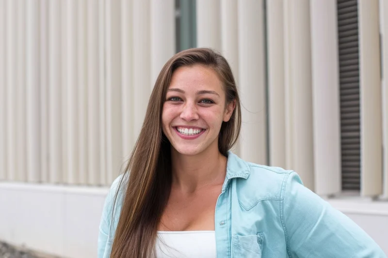 Smiling woman with long brown hair wearing light blue denim shirt outdoors