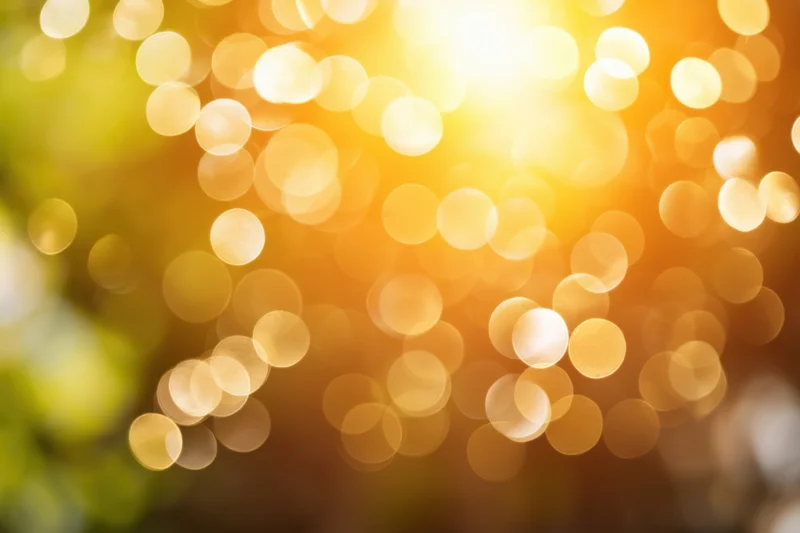 Golden bokeh light effect with soft glow and blurred green foliage in natural outdoor setting